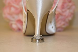 Wedding bands on bride's heels, with flowers in background.